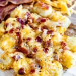 tater tots laid out on a cutting board and they are covered in cheese and bacon.