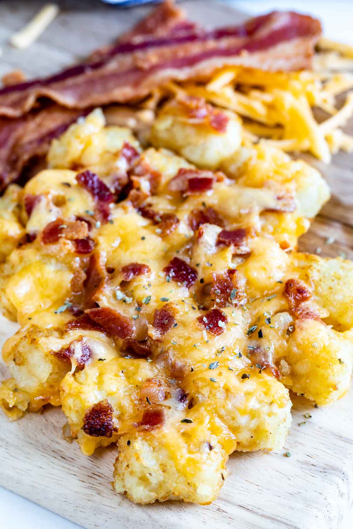 tater tots laid out on a cutting board and they are covered in cheese and bacon.