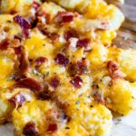 tater tots laid out on a cutting board and they are covered in cheese and bacon.