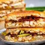 stacked sandwich with chicken and bacon and pickles in the center.