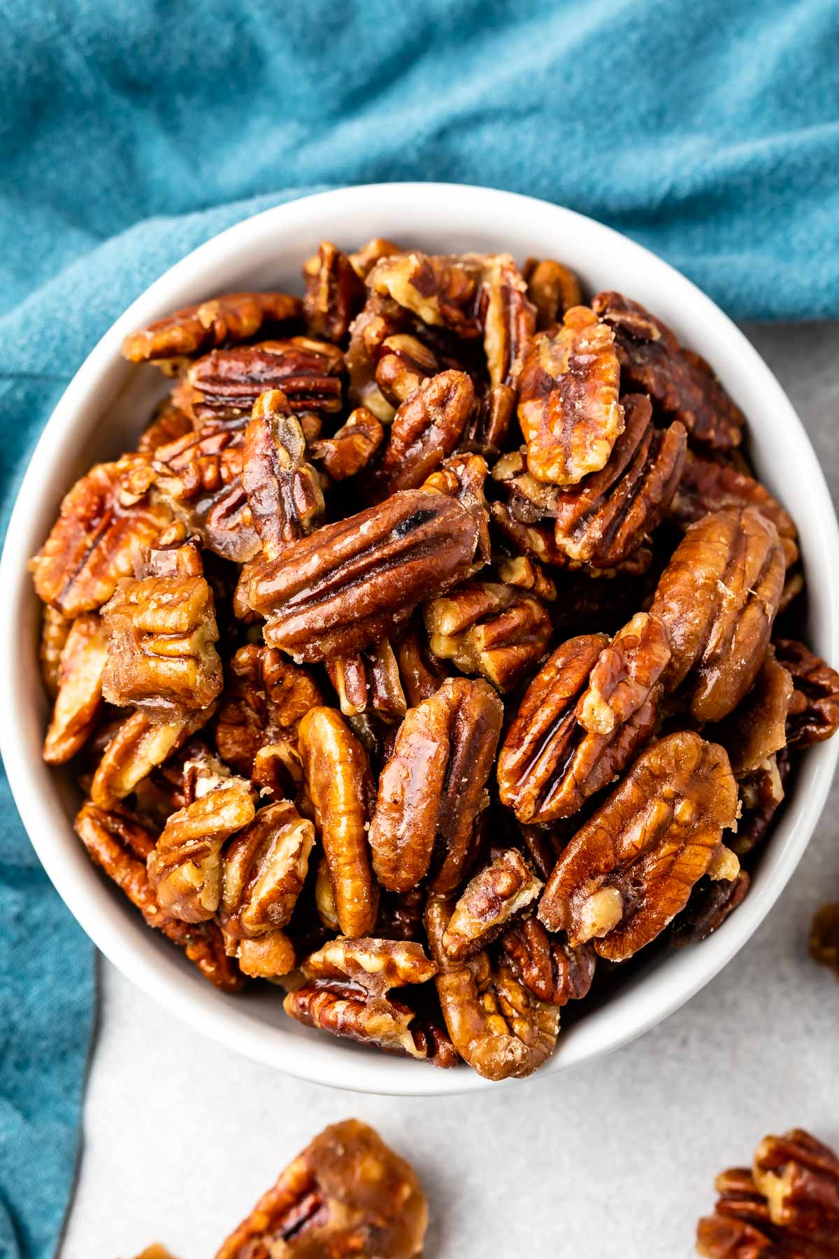 candied pecans in a white bowl next to a teal towel.