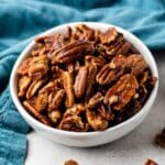 candied pecans in a white bowl next to a teal towel.