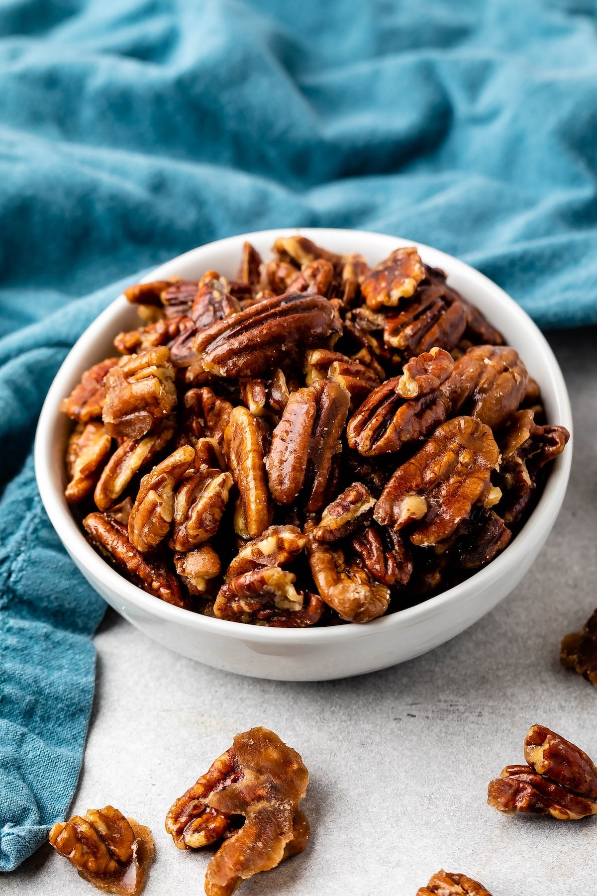 candied pecans in a white bowl next to a teal towel.