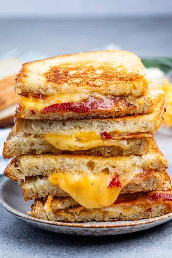 stacked grilled cheese slices with cheese and bacon pouring out the sides.