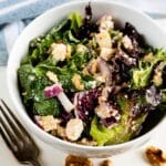 apples and walnuts and greens in a white bowl next to a wooden spoon.