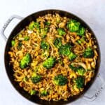 broccoli mixed with onions and mushrooms in a black pan.