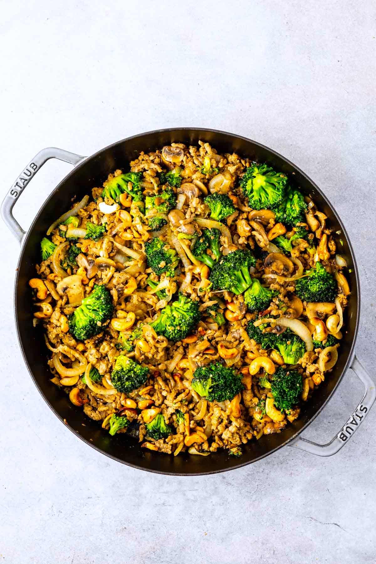 broccoli mixed with onions and mushrooms in a black pan.