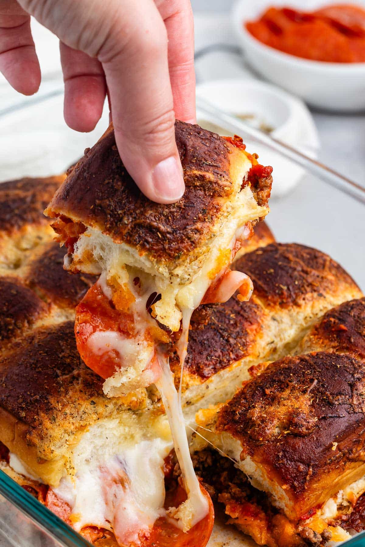 hand holding pizza slider from outside the clear pan.