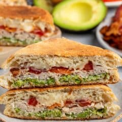 stacked sandwich with turkey and avocado and bacon between two halves of bread.