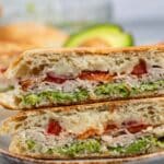 stacked sandwich with turkey and avocado and bacon between two halves of bread.