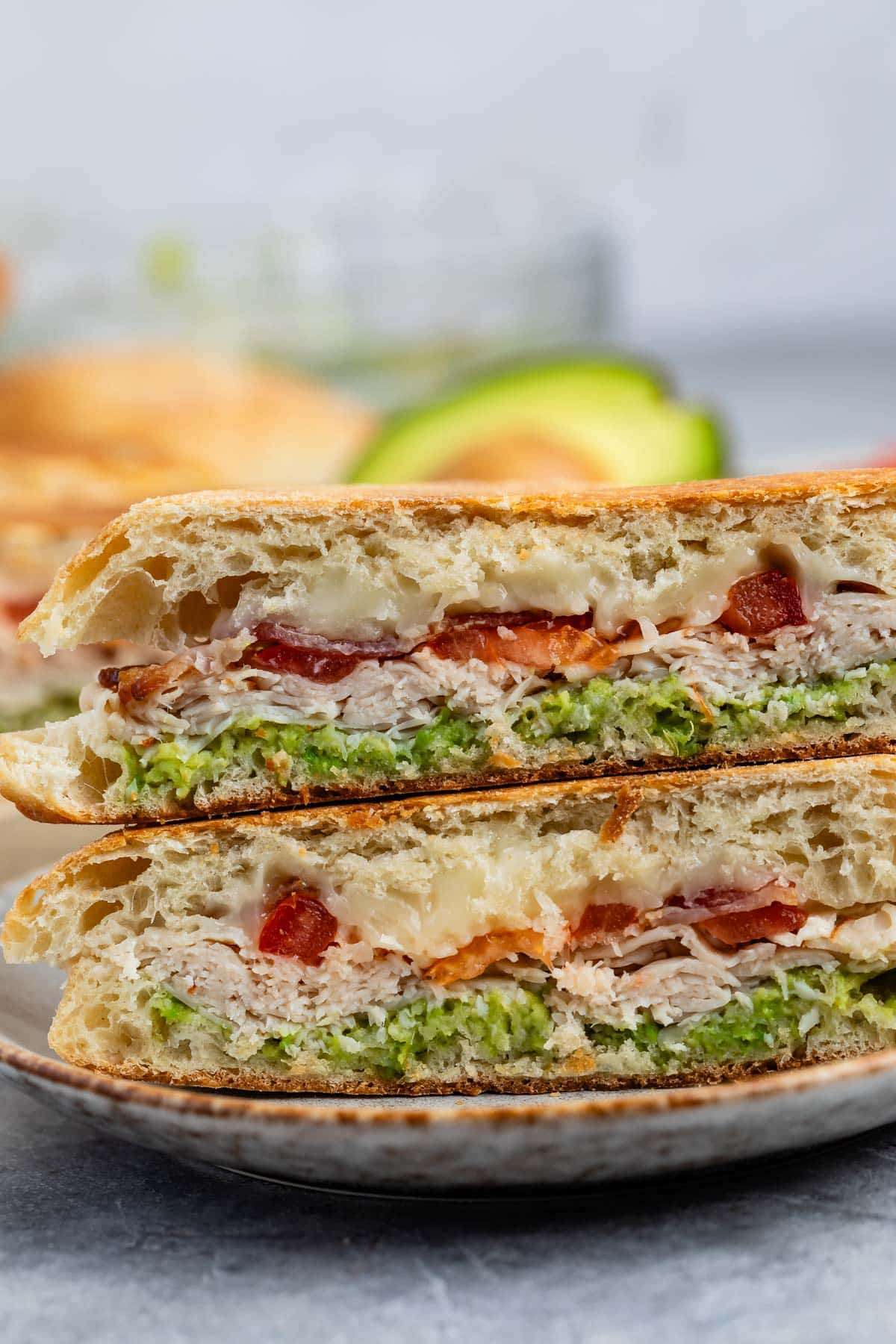 stacked sandwich with turkey and avocado and bacon between two halves of bread.