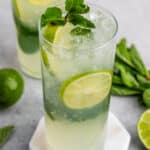 mojito in a tall clear class with sliced limes and mint leaves in the drink.