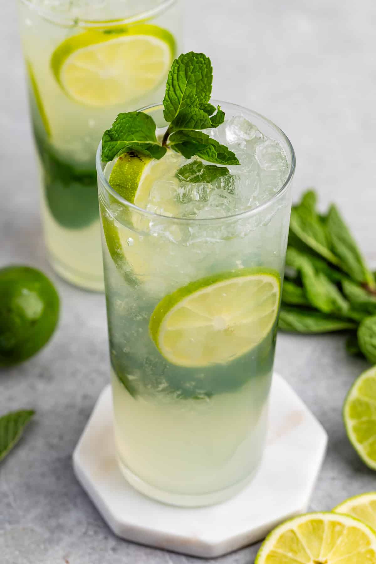 mojito in a tall clear class with sliced limes and mint leaves in the drink.