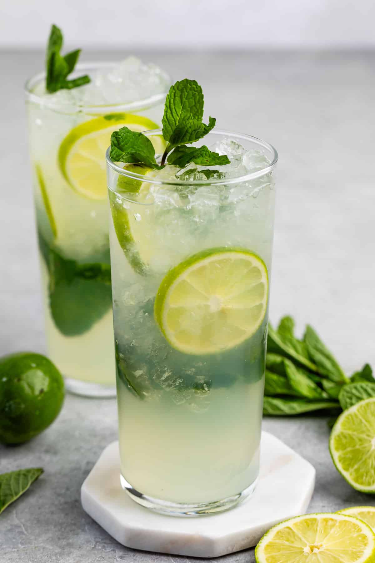 mojito in a tall clear class with sliced limes and mint leaves in the drink.