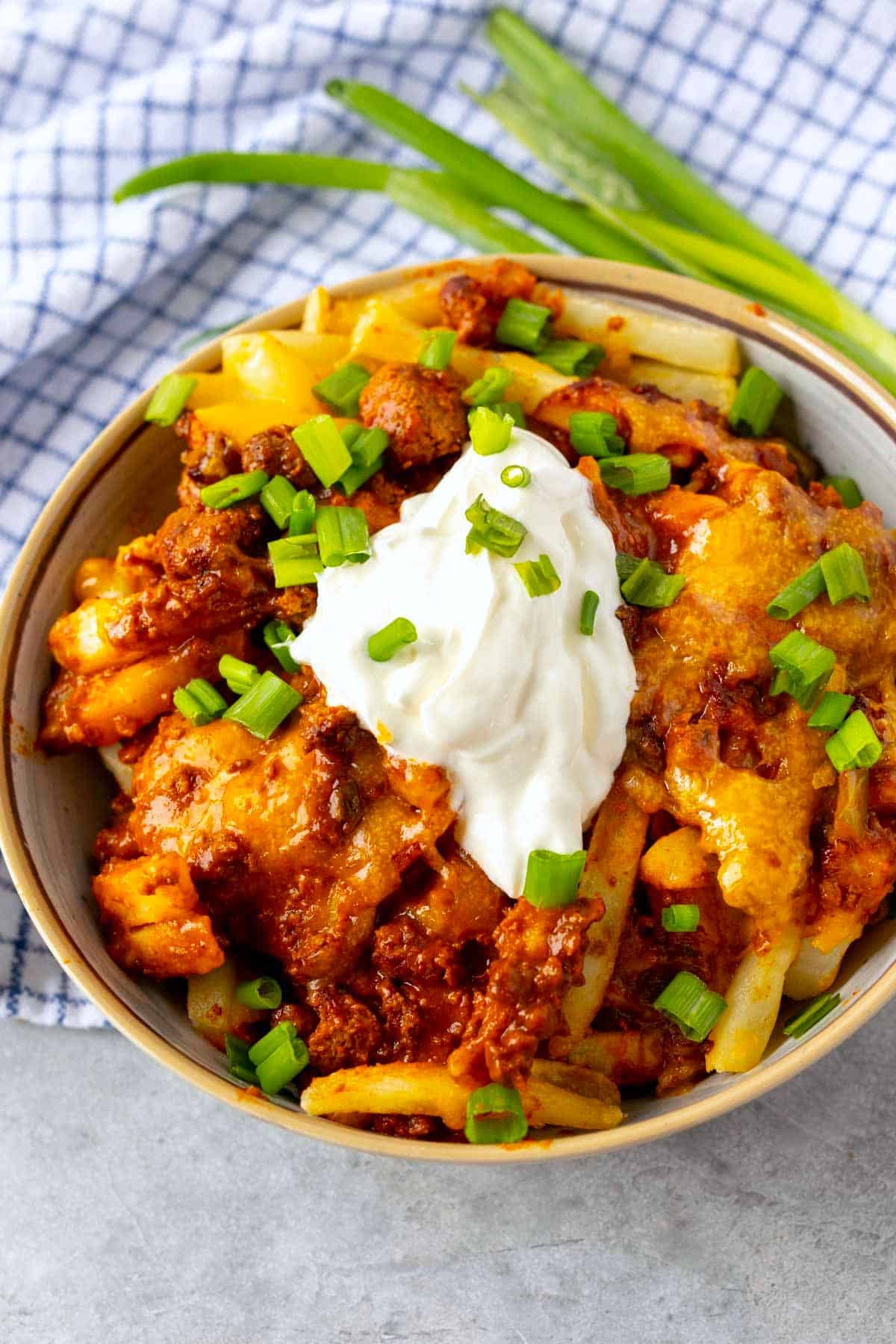 chili cheese fries in a grey bowl with sour cream on top.