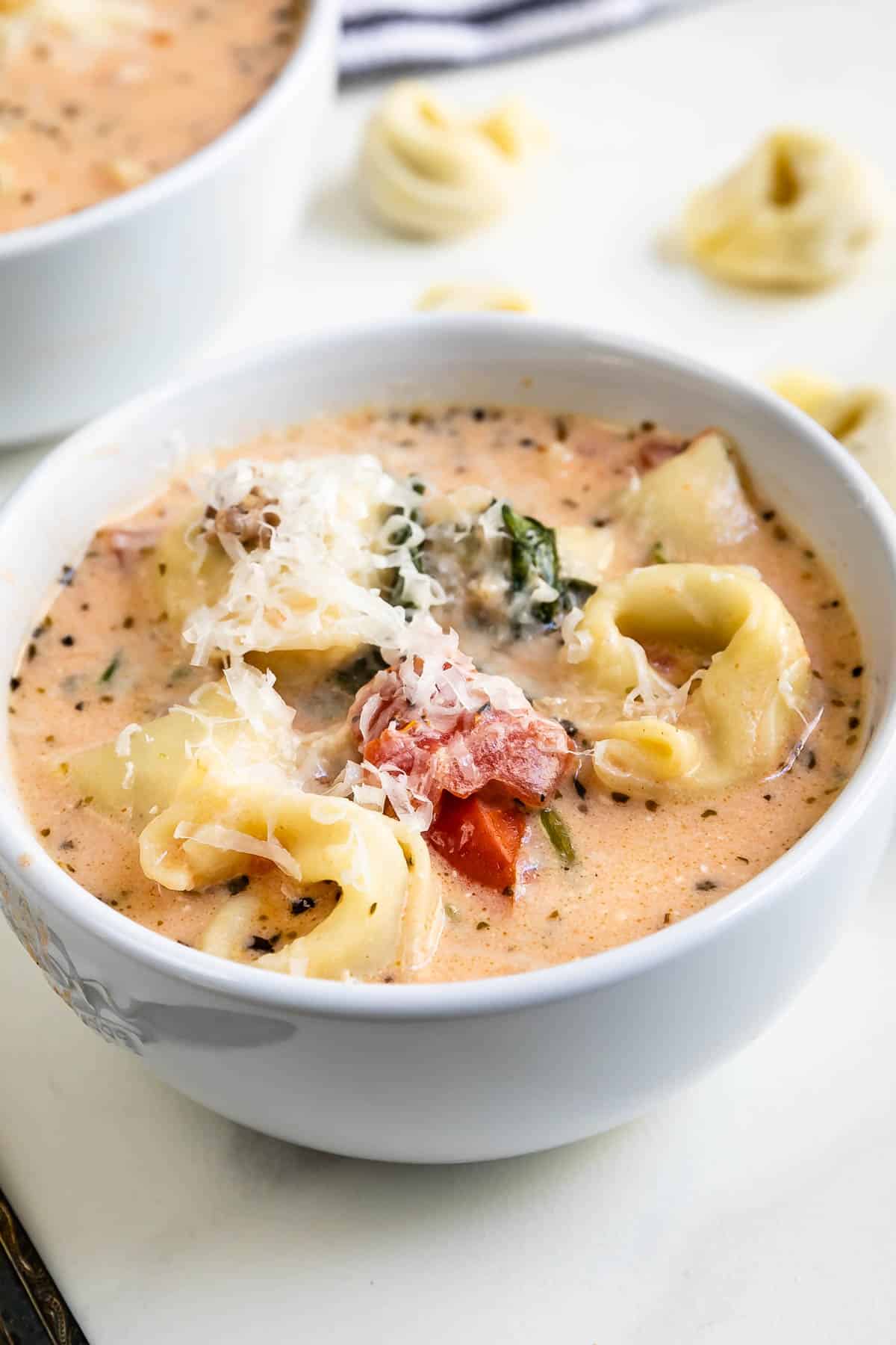 orange soup with tortellini in a white bowl.