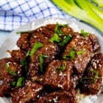 Mongolian beef on a white plate with green onion cut on top.