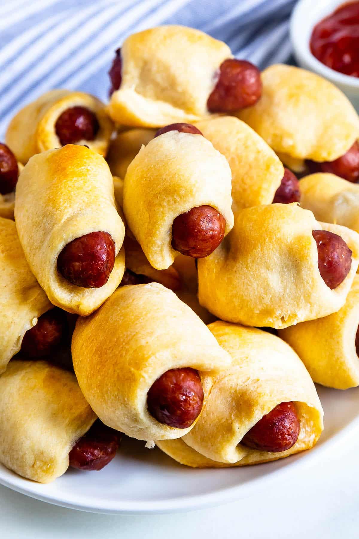 stacked pigs in a blanket laid out on a white plate.