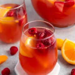 red drink in a clear glass with lemon and raspberries inside.