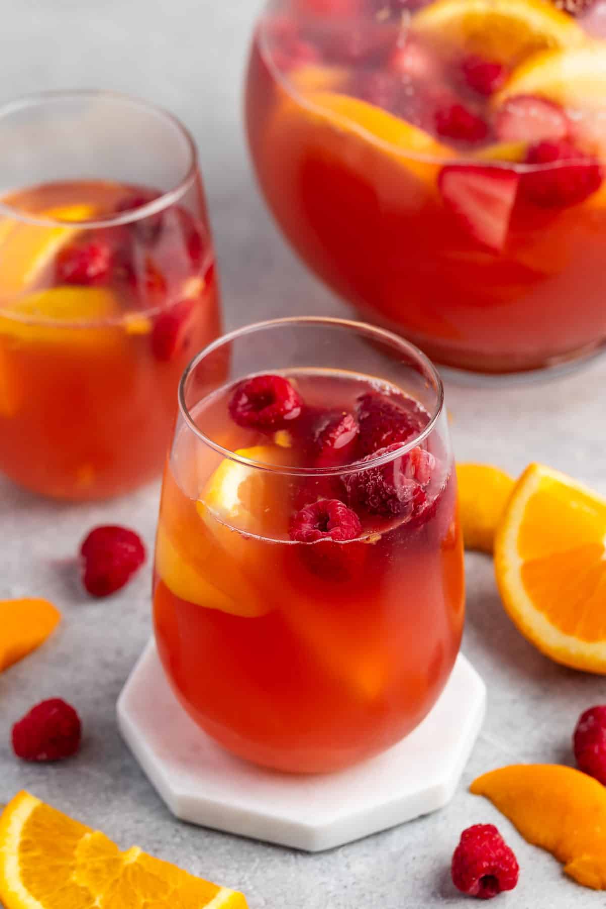 red drink in a clear glass with lemon and raspberries inside.