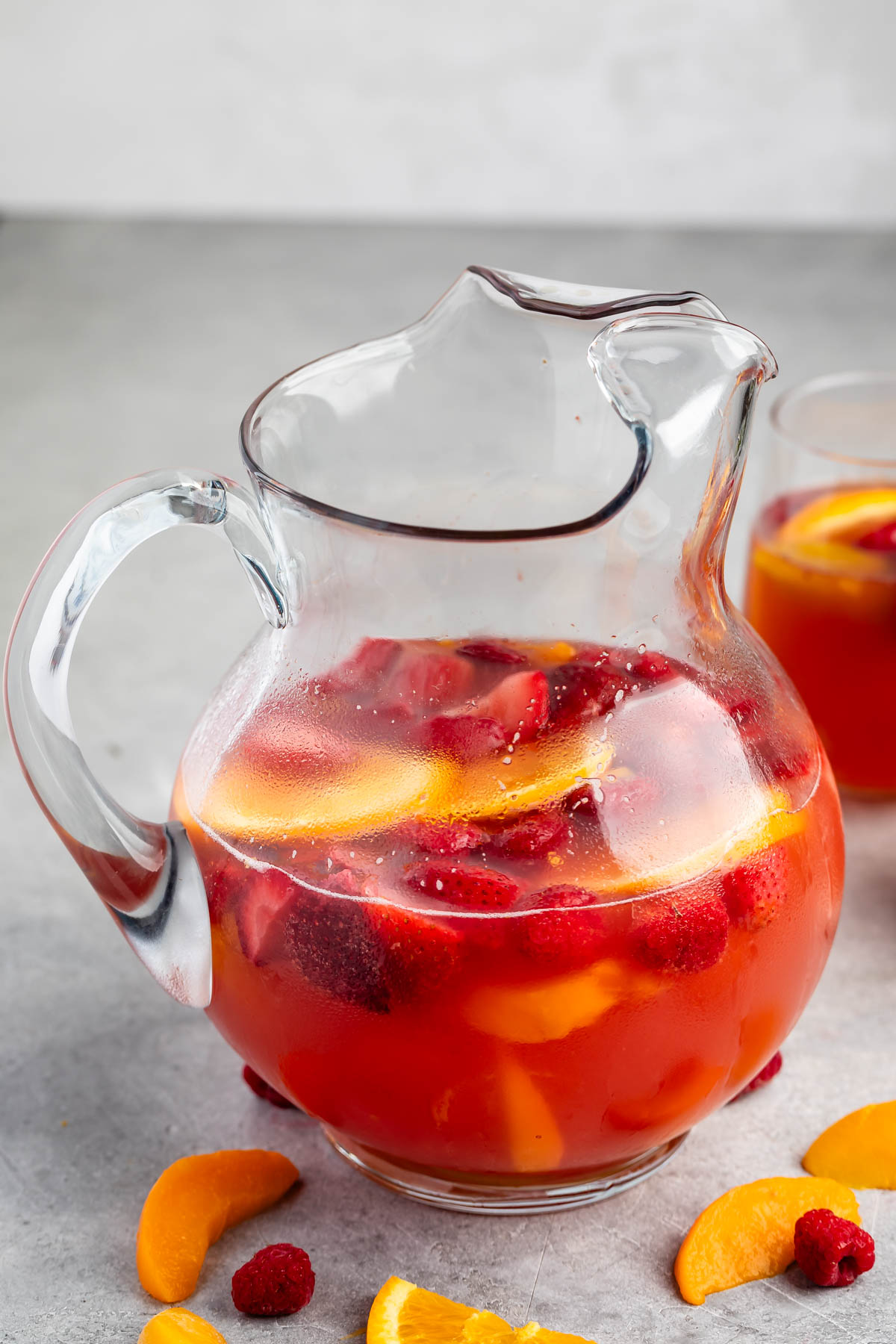 red drink in a clear glass with lemon and raspberries inside.