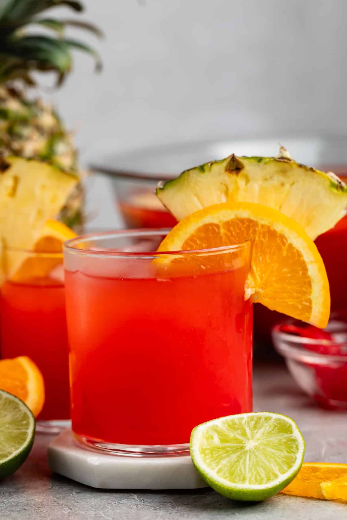 short clear glass with red drink inside and an orange and pineapple slice on the rim.