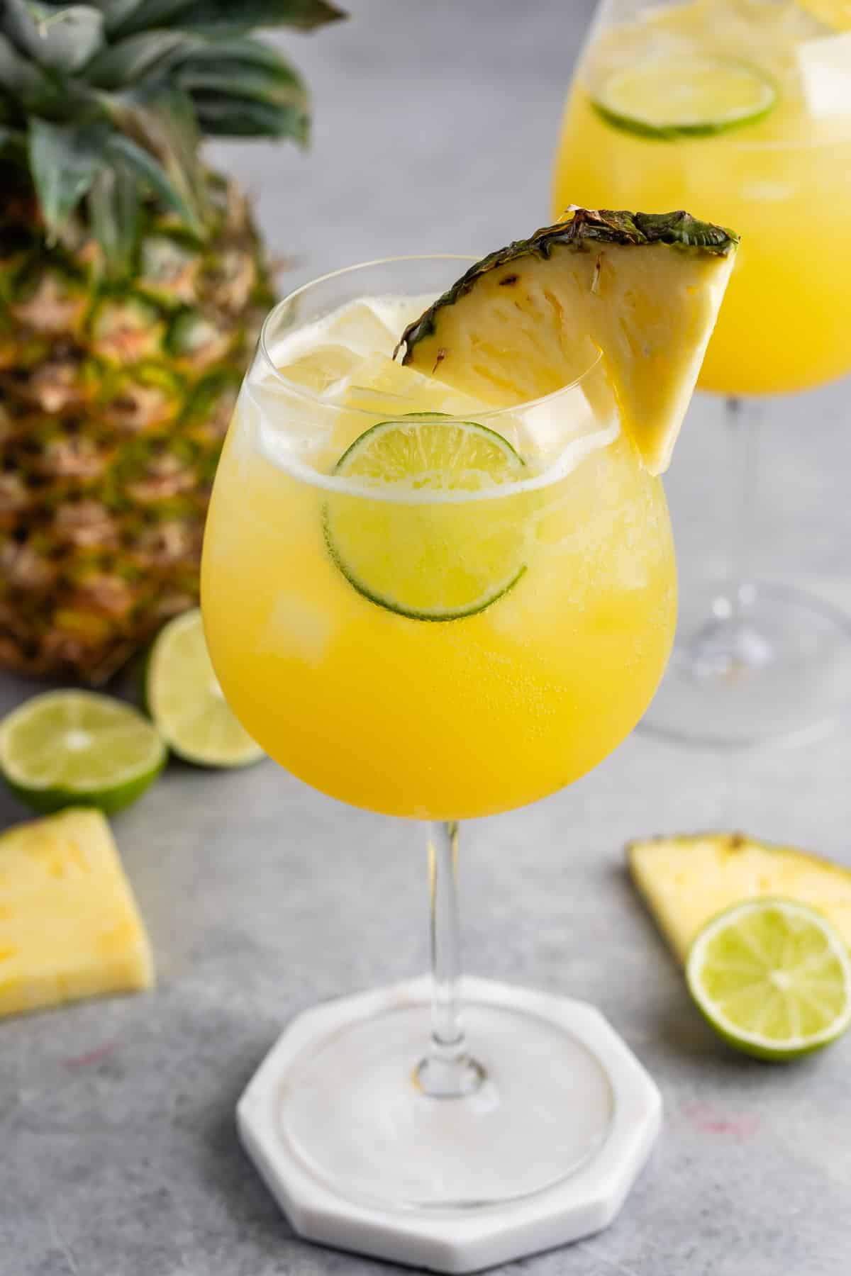 yellow drink in a tall clear glass with a pineapple wedge on the rim.