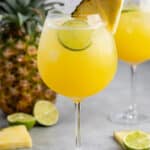 yellow drink in a tall clear glass with a pineapple wedge on the rim.