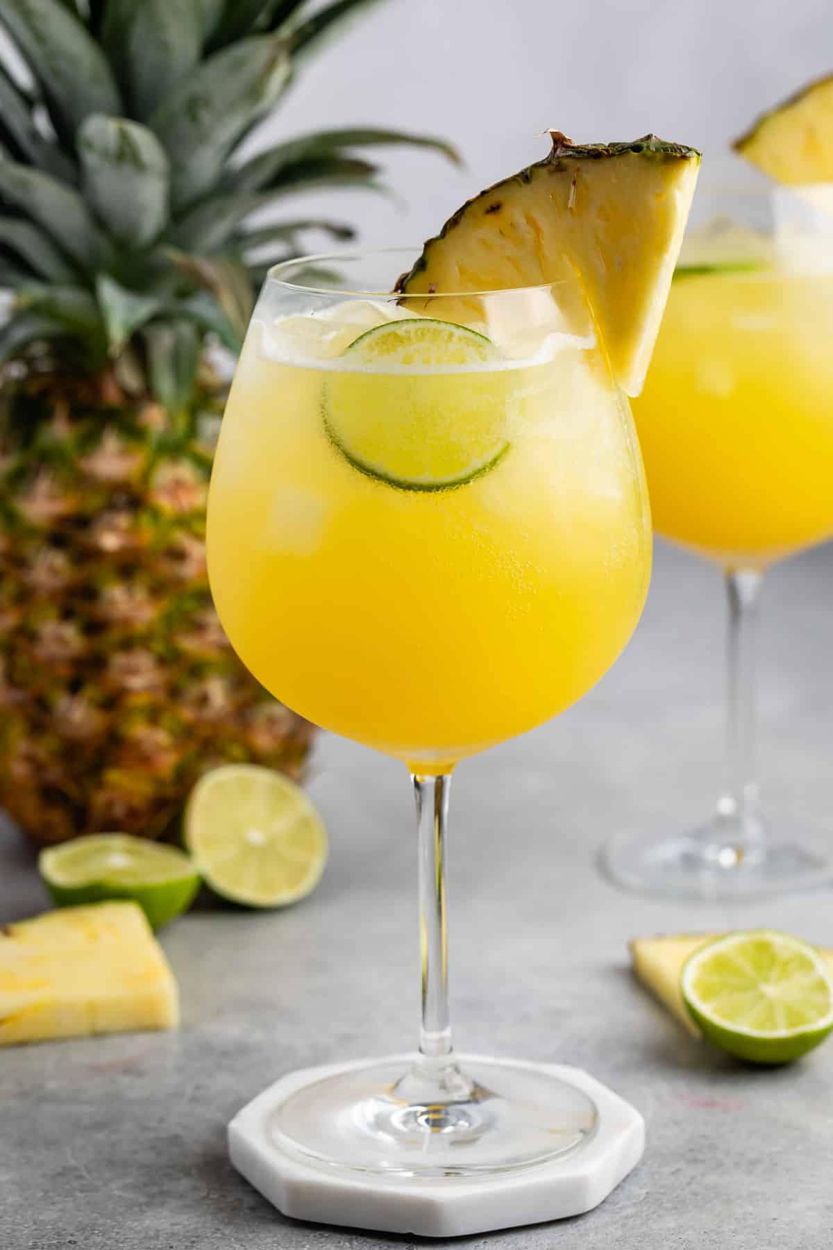 yellow drink in a tall clear glass with a pineapple wedge on the rim.