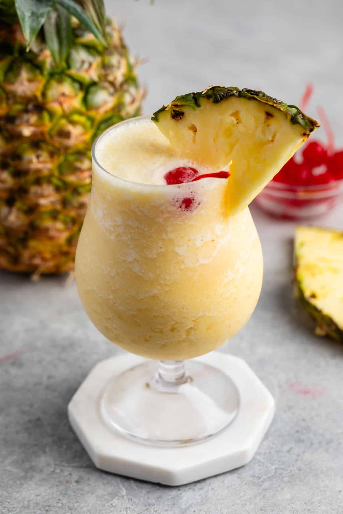 yellow Pina colada in a clear glass with a pineapple and cherry on the rim.