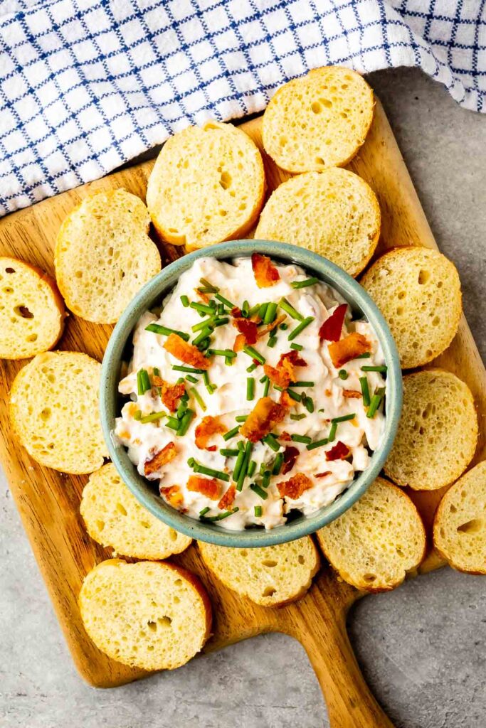 baked potato dip in a green bowl surrounded by sliced bread.