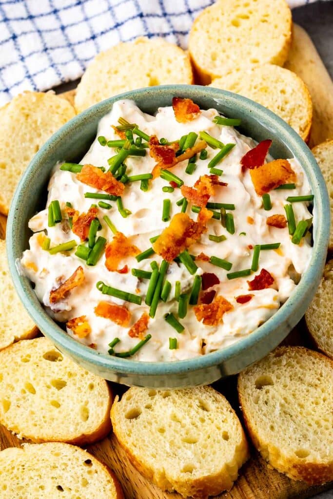 baked potato dip in a green bowl surrounded by sliced bread.