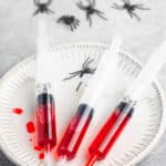 red grenedine in a plastic syringe laid out on a white plate next to fake spiders.