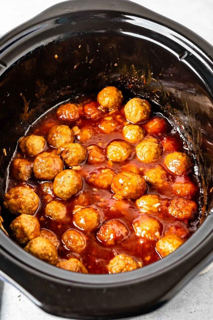 meatballs covered in sauce in a black crockpot.