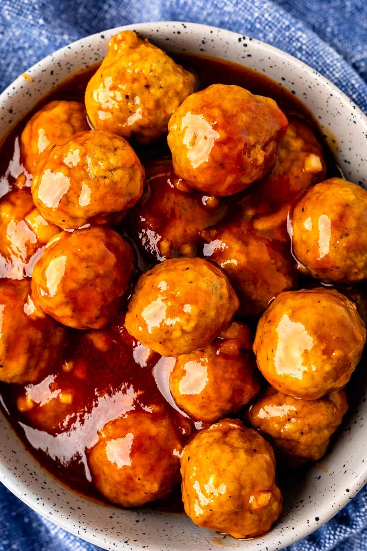 meatballs covered in sauce in a grey spotted bowl.