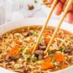 ramen being held up with chopsticks and topped with carrots and mushrooms and green onions.