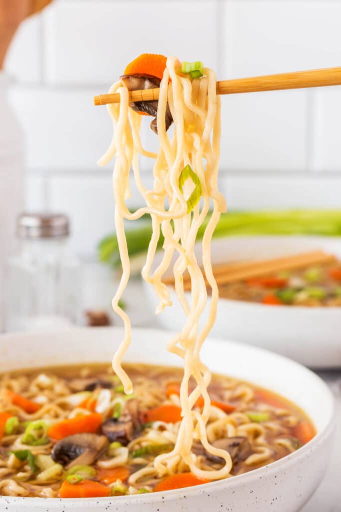 ramen being held up with chopsticks and topped with carrots and mushrooms and green onions.