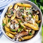 pasta and mushrooms mixed in a grey spotted bowl.