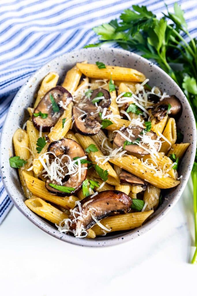 pasta and mushrooms mixed in a grey spotted bowl.