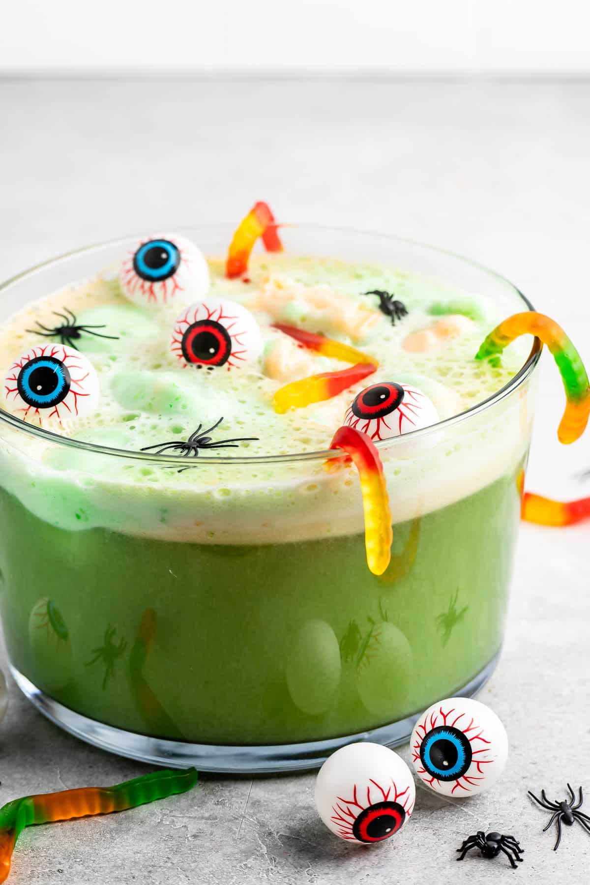 green punch in a large clear bowl with gummy worms and plastic spiders and eyeballs on top.