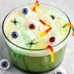 green punch in a large clear bowl with gummy worms and plastic spiders and eyeballs on top.