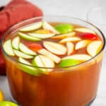 apple punch in a large clear bowl with sliced apples on top.