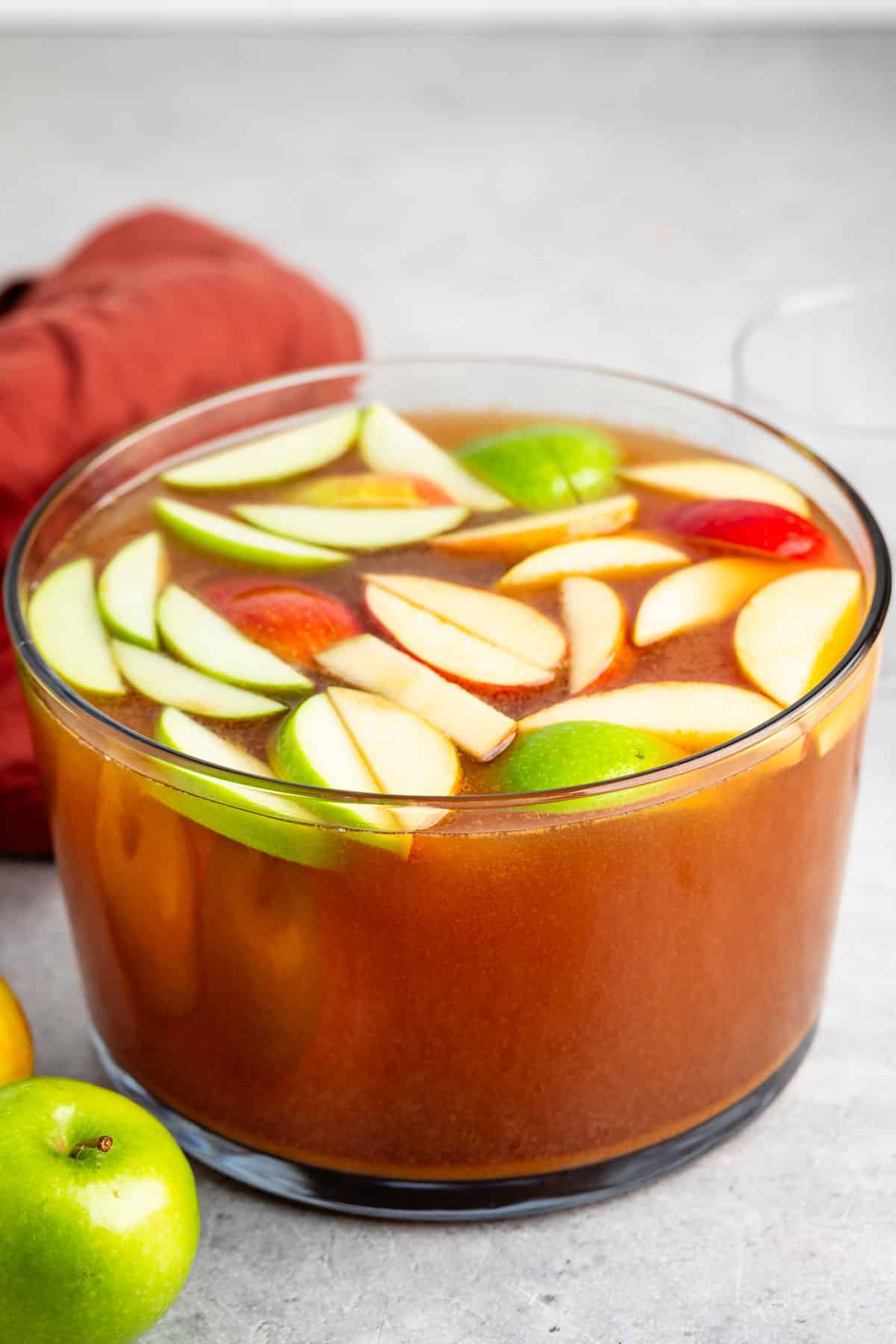 apple punch in a large clear bowl with sliced apples on top.