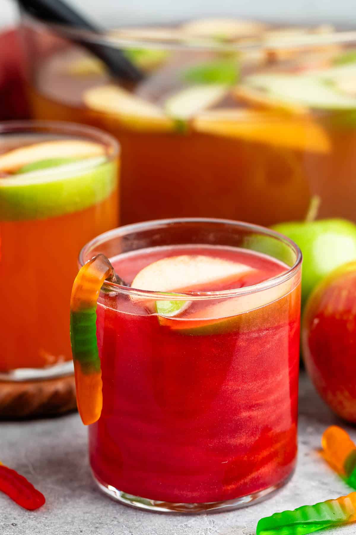 red poison apple punch in a clear glass with a gummy worm coming out the side.