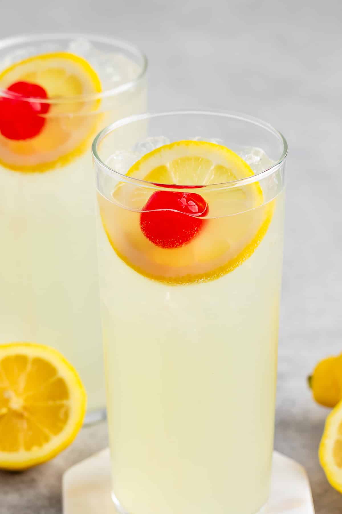 yellow drink mixed with a lemon slice and cherry in a tall clear glass.