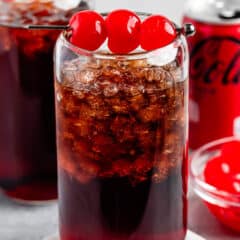 brown drink in a clear glass with cherries on top.