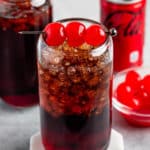 brown drink in a clear glass with cherries on top.