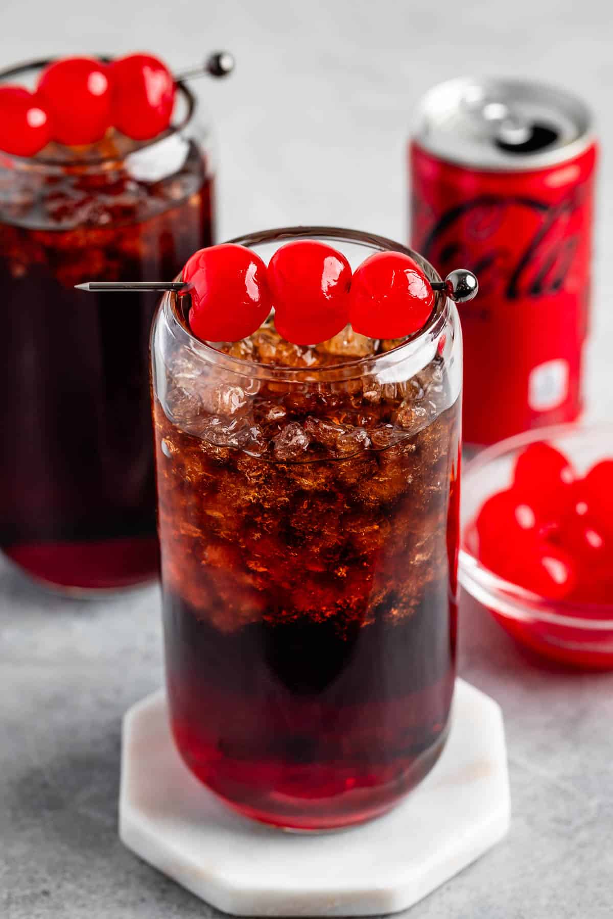 brown drink in a clear glass with cherries on top.