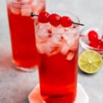 red drink in a tall clear glass with cherries on top.