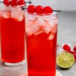 red drink in a tall clear glass with cherries on top.